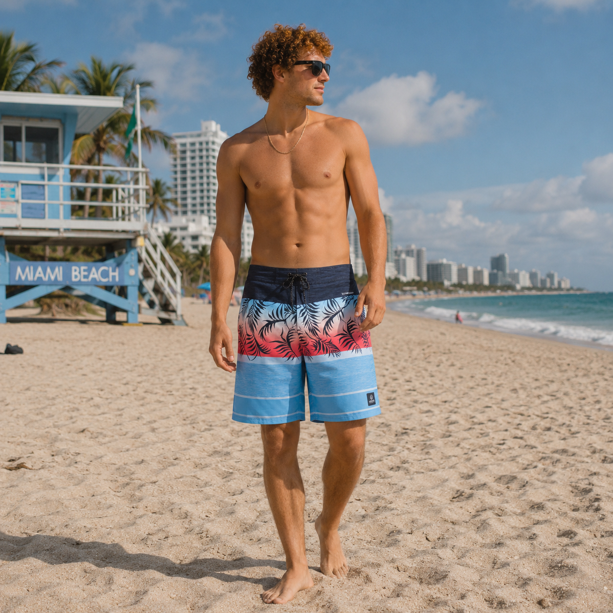 Man wearing colorful swim shorts on a beach with a city skyline in the background