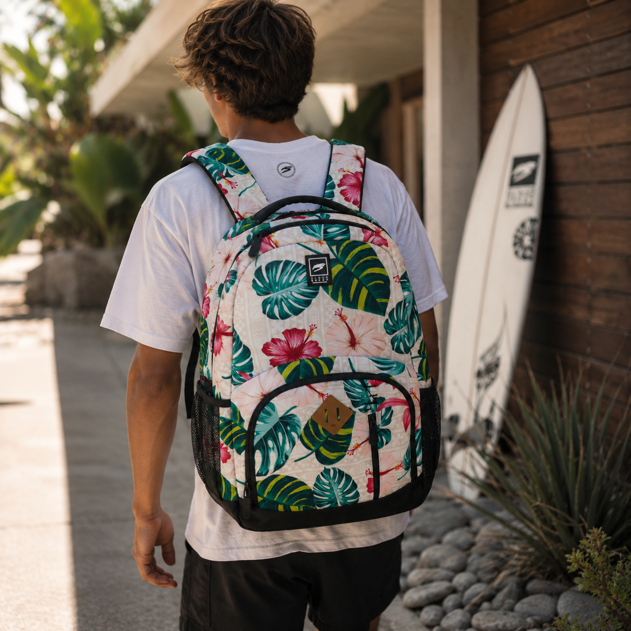 Male model uusing Sand tropical backpack with floral and palm print design. Lightweight everyday backpack for travel, school, beach, and casual use.